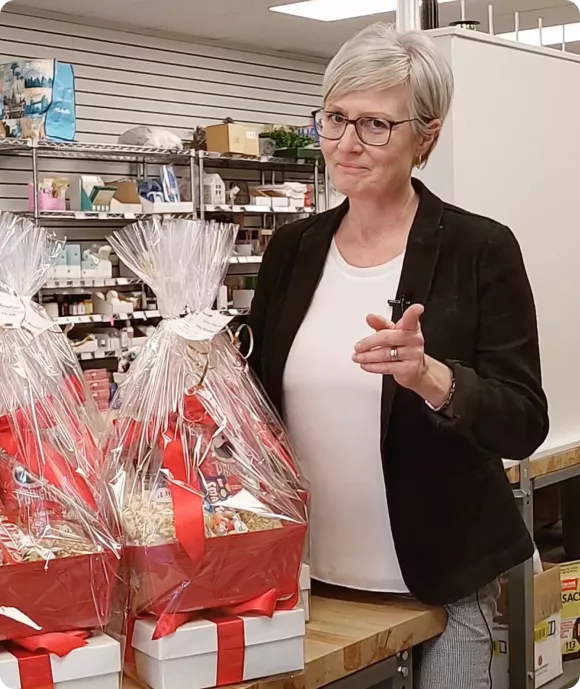Owner Noreen Ward standing in The Gift Designers studio with beautifully wrapped gift baskets, representing the brand’s personalized gifting services.
